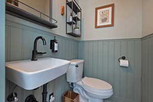 Bathroom with a sink, toilet, a wainscoted wall, and a decorative wall