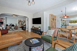 Living room with a desk, arched walkways, ceiling fan, wood finished floors, and built in shelves