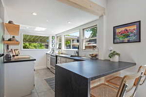 Kitchen with a sink, dark countertops, open shelves, a peninsula, and plenty of natural light
