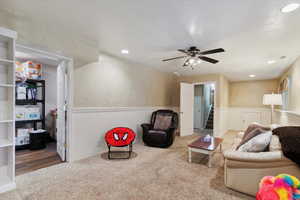 Carpeted living area with a wainscoted wall, stairway, ceiling fan, and recessed lighting