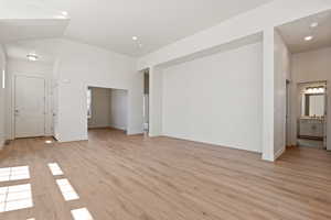 Unfurnished living room with light wood-style flooring, lofted ceiling, baseboards, and recessed lighting