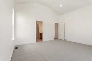 Unfurnished bedroom featuring light carpet, baseboards, high vaulted ceiling, and ensuite bathroom