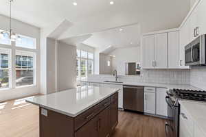 Kitchen with stainless steel appliances, a sink, light wood-style floors, light countertops, and decorative backsplash