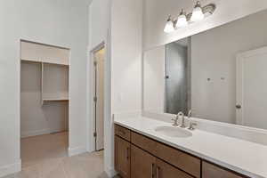 Bathroom featuring a walk in closet, vanity, a stall shower, baseboards, and tile patterned flooring