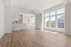 Unfurnished living room featuring light wood-type flooring, baseboards, a chandelier, recessed lighting, and a towering ceiling