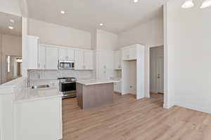 Kitchen featuring stainless steel appliances, a sink, backsplash, light wood-style flooring, and a center island
