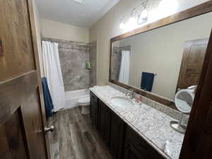Full bathroom with double vanity, wood finished floors, shower / bath combination with curtain, toilet, and a textured ceiling