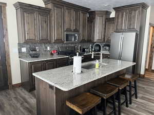 Kitchen with appliances with stainless steel finishes, a sink, dark wood finished floors, dark brown cabinetry, and decorative backsplash