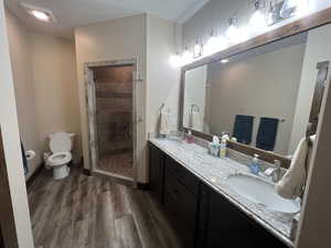 Full bathroom featuring toilet, wood finished floors, double vanity, and a stall shower