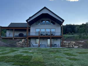Back of house with a yard, a shingled roof, a patio, board and batten siding, and a wooden deck