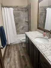 Bathroom with vanity, toilet, shower / bath combination with curtain, and wood finished floors