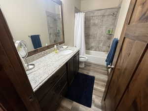 Bathroom featuring toilet, shower / tub combo, vanity, and wood finished floors