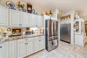 Kitchen featuring freestanding refrigerator, white cabinets, and light stone counters