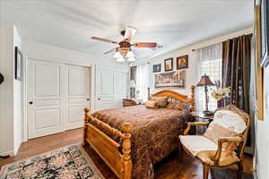 Bedroom with two closets, wood finished floors, and a ceiling fan