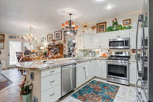 Kitchen with stainless steel appliances, a chandelier, a peninsula, white cabinets, and vaulted ceiling