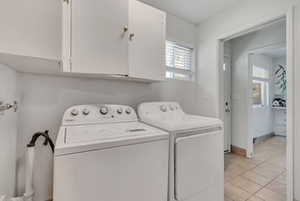 Laundry room featuring cabinet space, independent washer and dryer, light tile patterned floors, and baseboards
