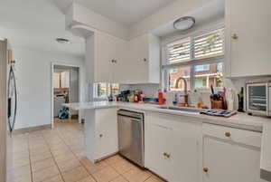 Kitchen with appliances with stainless steel finishes, light countertops, light tile patterned floors, white cabinets, and a peninsula