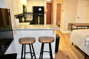 Kitchen with black appliances, a peninsula, light wood finished floors, white cabinets, and light stone counters