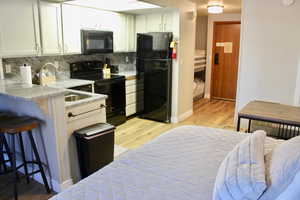 Kitchen with black appliances, backsplash, white cabinets, light wood-type flooring, and a breakfast bar area