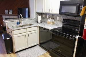 Kitchen featuring black appliances, a sink, light wood-style flooring, backsplash, and light stone counters