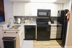 Kitchen featuring black appliances, a sink, light wood-type flooring, tasteful backsplash, and white cabinets