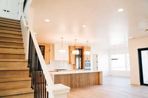 Kitchen with light countertops, stainless steel double oven, a spacious island, light wood-style floors, and recessed lighting