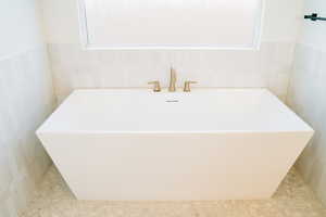 Full bathroom featuring a soaking tub, tile walls, and healthy amount of natural light