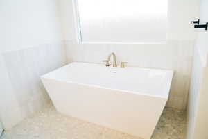 Full bathroom featuring tile walls, a freestanding bath, and wainscoting