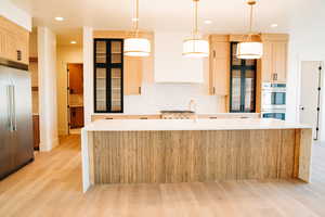 Kitchen featuring stainless steel appliances, light wood-style flooring, light brown cabinetry, a center island with sink, and light countertops