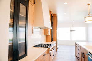 Kitchen with premium range hood, appliances with stainless steel finishes, light wood-type flooring, hanging light fixtures, and light stone countertops