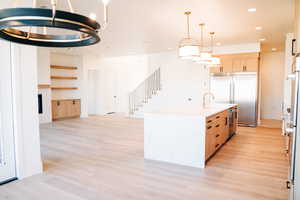 Kitchen with appliances with stainless steel finishes, light brown cabinetry, light wood-style floors, recessed lighting, and a fireplace
