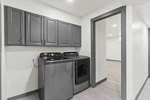 Laundry room with washer and dryer, light wood finished floors, baseboards, and cabinet space