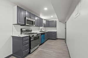 Kitchen featuring stainless steel appliances, a sink, light countertops, baseboards, and light wood-style floors