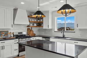 Kitchen featuring appliances with stainless steel finishes, wall chimney exhaust hood, a sink, dark countertops, and recessed lighting