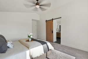 Carpeted bedroom featuring a barn door, baseboards, lofted ceiling, connected bathroom, and a ceiling fan