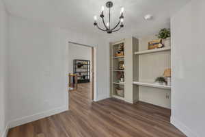Unfurnished dining area featuring a chandelier, dark wood-style floors, baseboards, and built in features