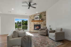 Living room featuring a stone fireplace, a ceiling fan, wood finished floors, vaulted ceiling, and baseboards
