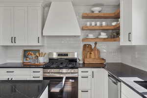 Kitchen featuring stainless steel appliances, exhaust hood, backsplash, and open shelves