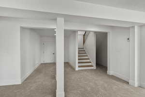 Finished below grade area featuring carpet flooring, baseboards, stairway, and a textured ceiling