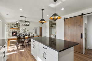 Kitchen featuring wood finished floors, dark countertops, a stone fireplace, a barn door, and recessed lighting