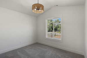 Carpeted spare room featuring vaulted ceiling, baseboards, and a chandelier