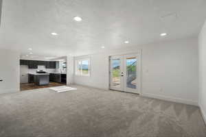 Unfurnished living room featuring carpet floors, baseboards, a textured ceiling, recessed lighting, and a sink