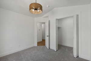Unfurnished bedroom with carpet flooring, a chandelier, lofted ceiling, baseboards, and a spacious closet