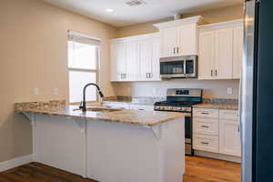 Kitchen with stainless steel appliances, a sink, a peninsula, white cabinets, and recessed lighting