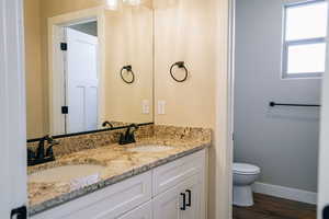 Bathroom featuring double vanity, toilet, baseboards, and wood finished floors