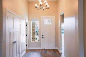 Foyer entrance with a chandelier, wood-type flooring, a high ceiling, and baseboards