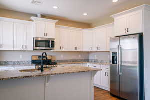 Kitchen with appliances with stainless steel finishes, recessed lighting, white cabinets, wood finished floors, and light stone counters