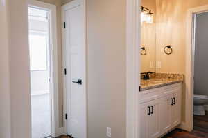 Bathroom featuring toilet, vanity, baseboards, and wood finished floors