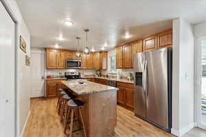 Kitchen with stainless steel appliances, light wood-style flooring, a center island, a breakfast bar, and a textured ceiling
