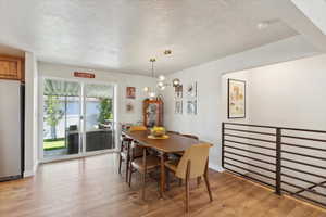 Dining area featuring a textured ceiling, light wood-type flooring, a chandelier, and baseboards